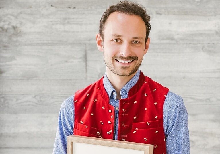 Roman Neustifter strahlt und hält einen Fotorahmen mit der Urkunde "Sonderpreis" TOP Heuriger in der Hand.