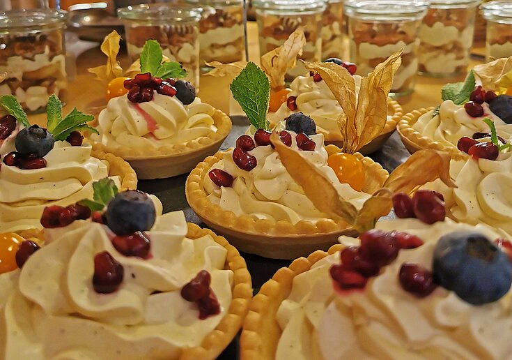 Muttertagsbrunch Vanilletörtchen In kleinen Schüsselchen auf Mürbteig ist eine weiße Vanillecreme mit verschiedenen Früchten oben drauf. Die Törtchen stehen auf einem Buffet.
