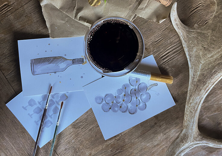 Drink x Create Weihnachten Ein Glas mit Rotwein gefüllt, rundherum liegen selbst gestaltete Weihnachtskarten.