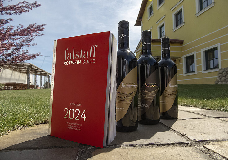 Das Falstaff Magazin steht mit drei Weinflaschen vom Weingut Neustifter im Gastgarten der Familie Neustifter.