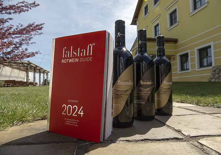 Das Falstaff Magazin steht mit drei Weinflaschen vom Weingut Neustifter im Gastgarten der Familie Neustifter.