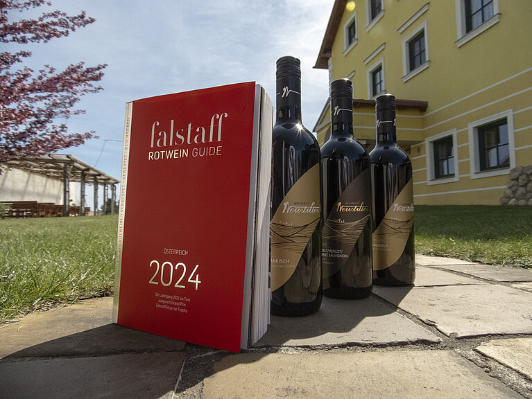 Das Falstaff Magazin steht mit drei Weinflaschen vom Weingut Neustifter im Gastgarten der Familie Neustifter.