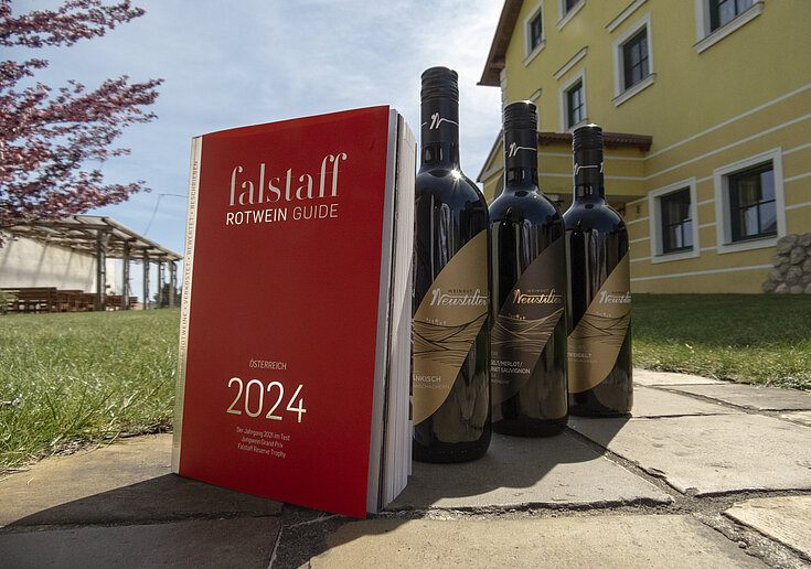 Das Falstaff Magazin steht mit drei Weinflaschen vom Weingut Neustifter im Gastgarten der Familie Neustifter.